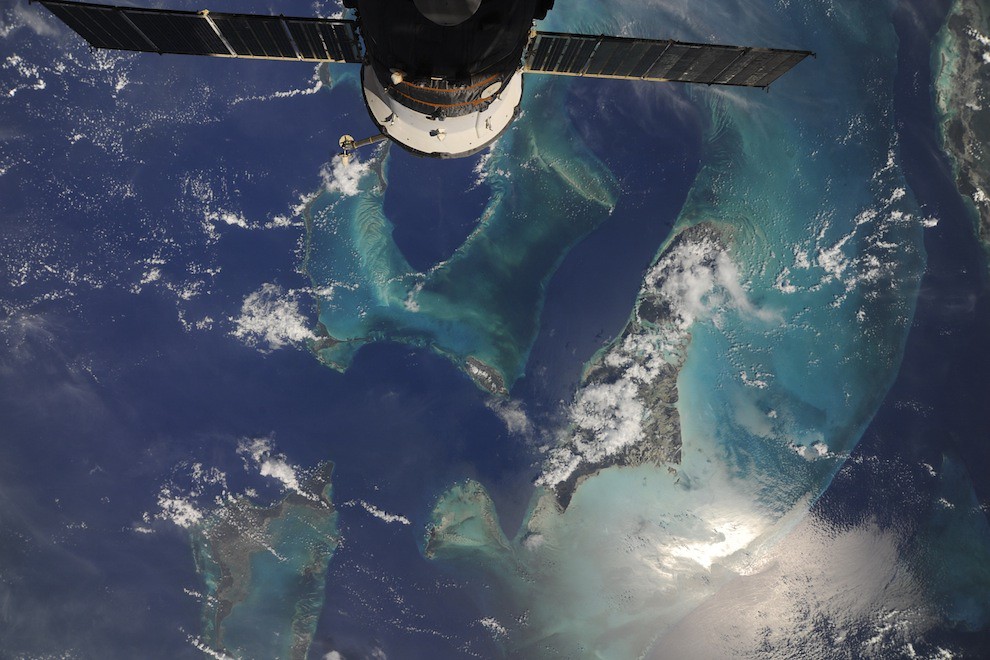 a view of Earth from space showing turquoise and dark blue coastal waters with islands and clouds